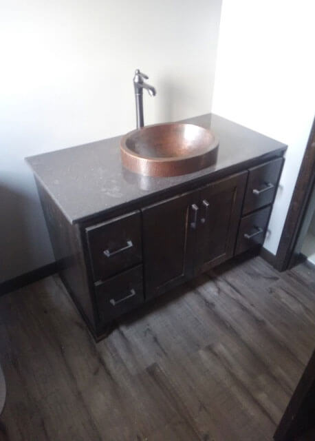 A brown raised bowl sink in a dark wood cabinet