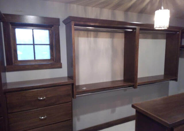 A grey closet with a window and dark wooden shelving