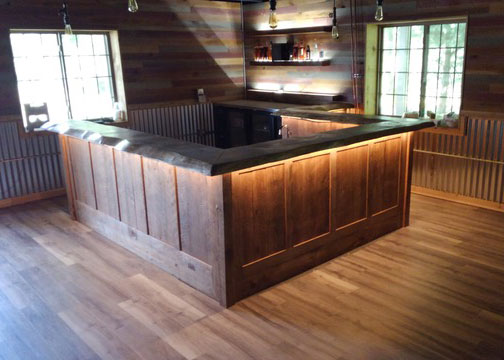 A room with a bar, pallette wood walls, and a hardwood floor