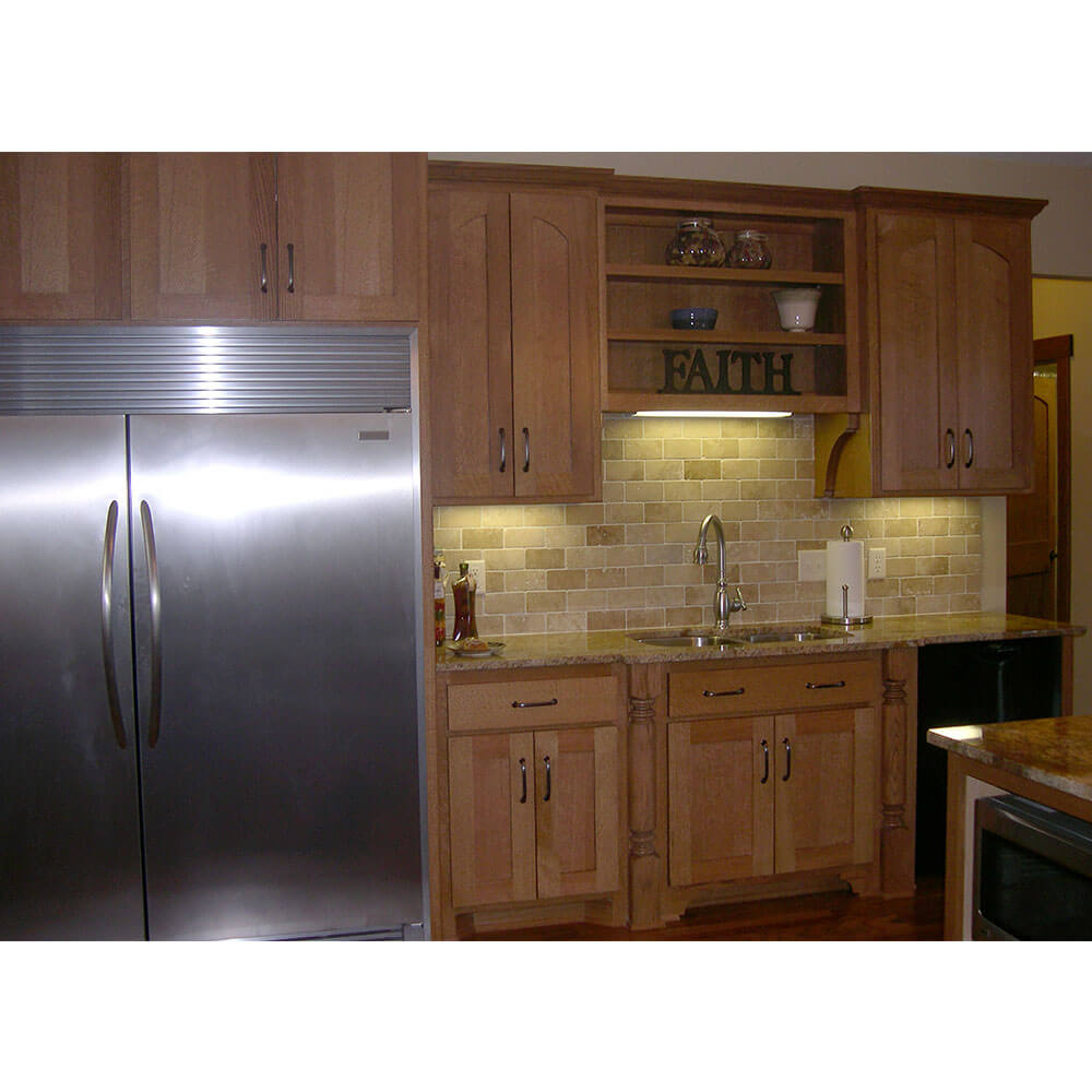 Tan brick wall behind wood cabinets and a large silver fridge